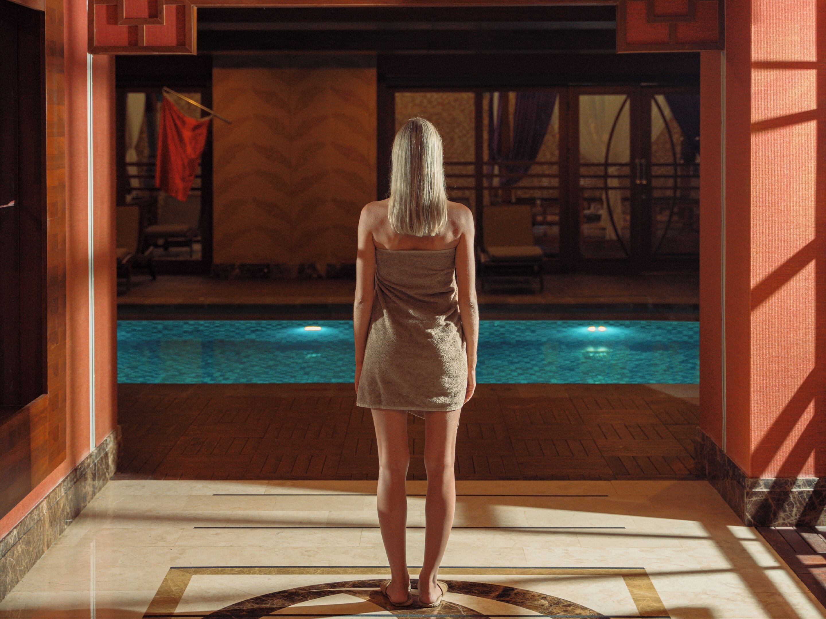 A person standing in a hallway with a pool visible through a glass door.