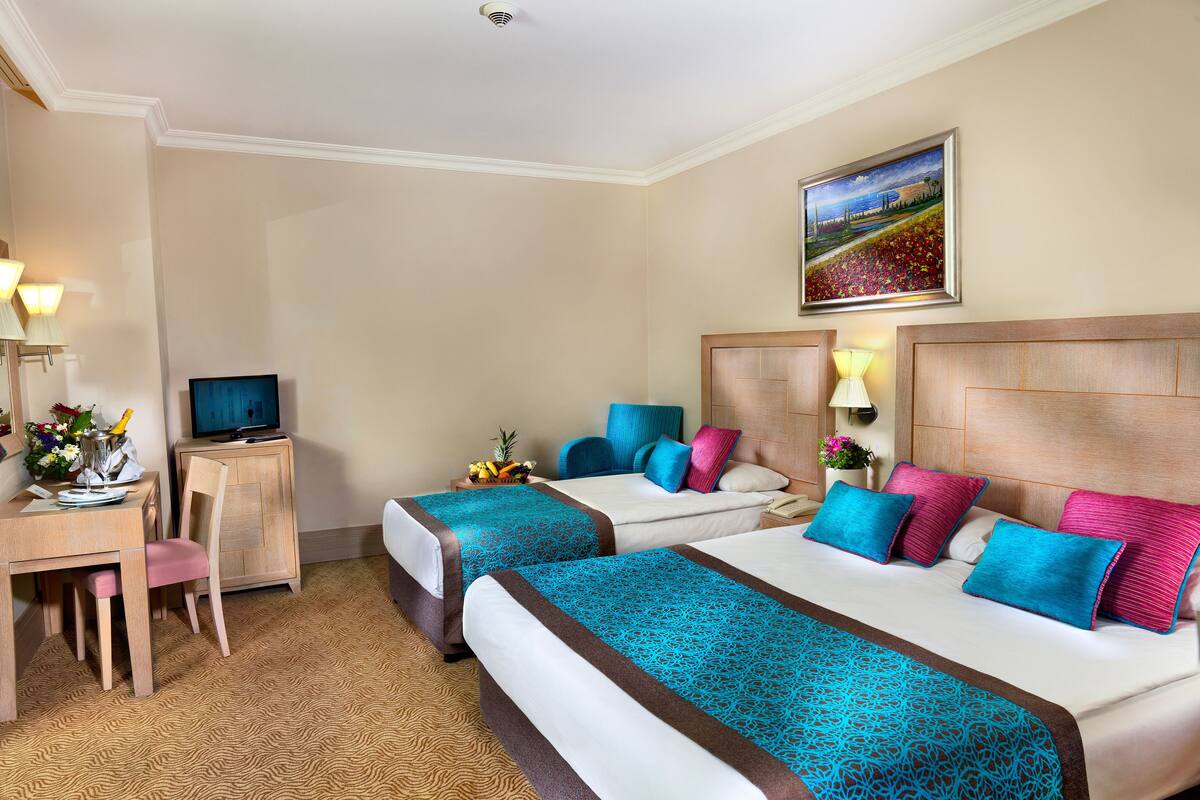 Une chambre d’hôtel avec deux lits, un bureau avec une télévision, une chaise et un tableau au mur.