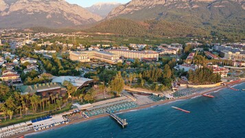 An aerial view of a coastal town with a marina, hotel buildings, and mountainous backdrop.