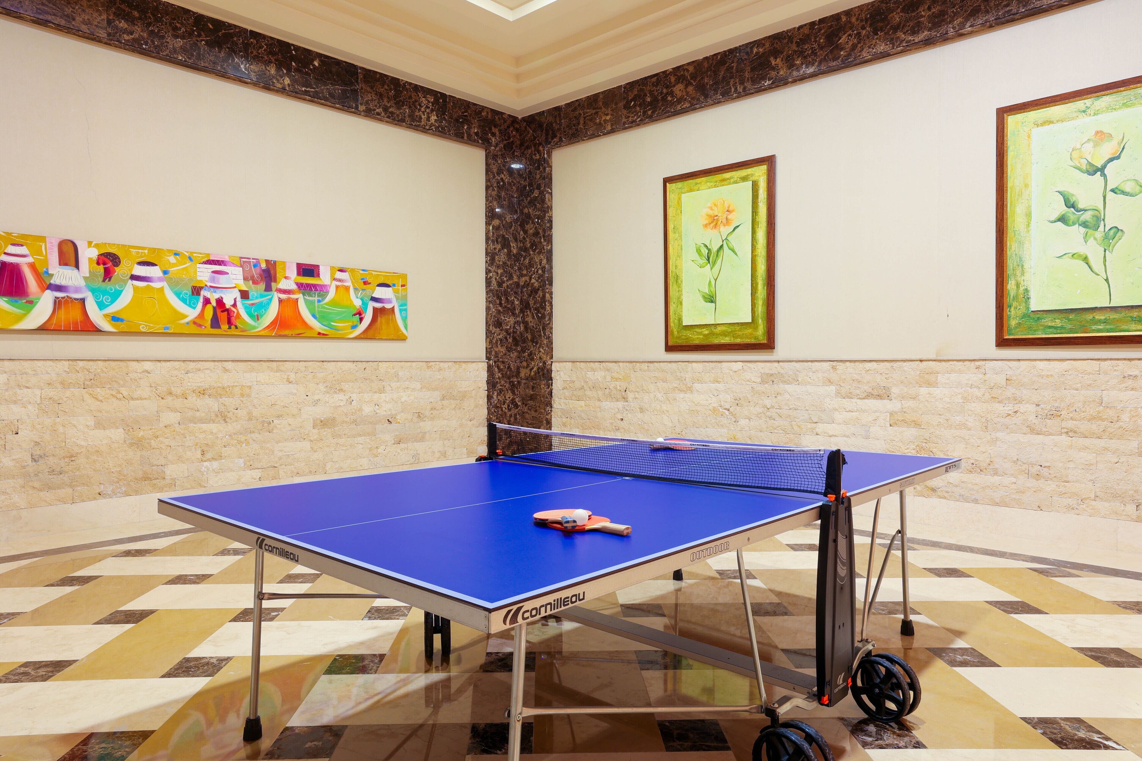 A ping pong table in a room with a checkered floor, a marble column, and colorful artwork on the walls.