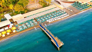 An aerial view of a beachside resort with a pier, rows of sun loungers, and umbrellas.