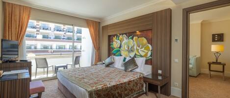 A hotel room with a large bed, a desk with a TV, a chair, and a balcony view.