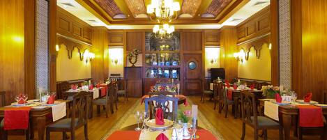 Un comedor formal con varias mesas dispuestas para el servicio, paneles de madera y una araña.