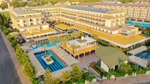 A hotel with multiple swimming pools, outdoor seating areas, and a large building with a flat roof.