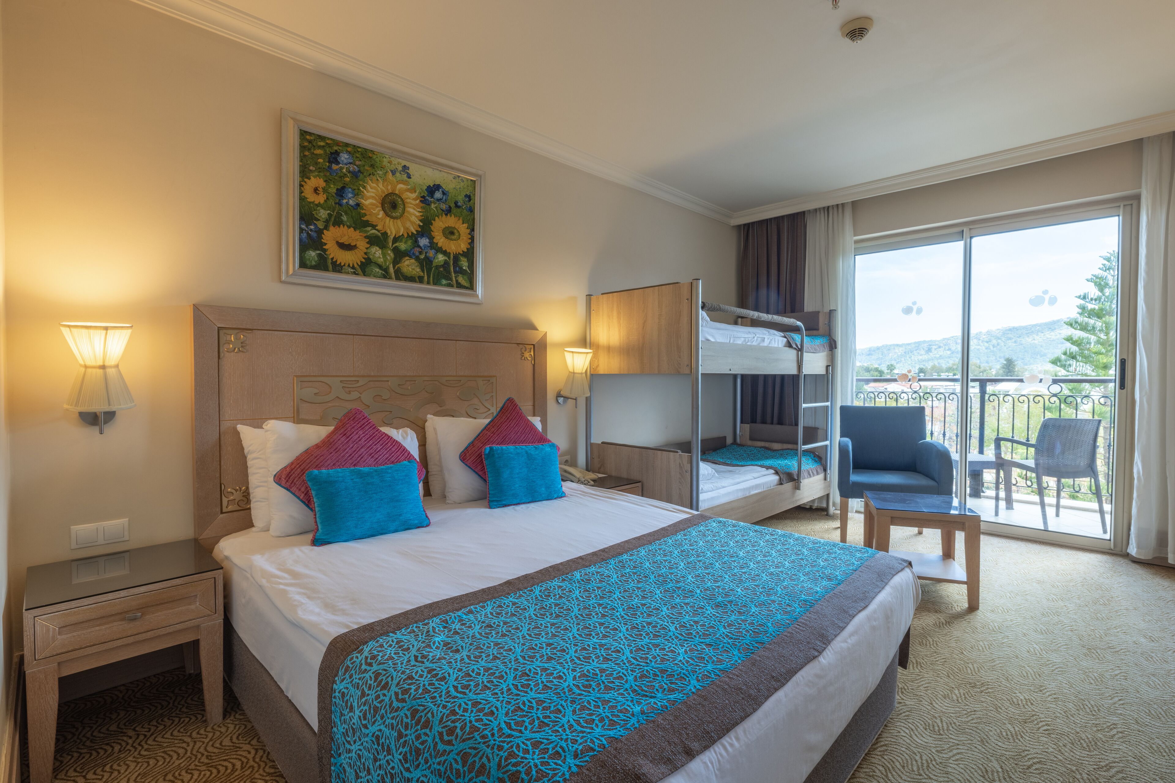 Habitación de hotel con una cama grande, una cama litera, un escritorio, una silla y un balcón con vistas.