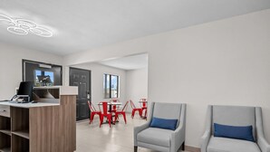 A modern hotel lobby with a reception desk, two armchairs with blue cushions, a dining area with red chairs, and a large window providing natural light. - Econo Lodge Biloxi Beach (Biloxi)