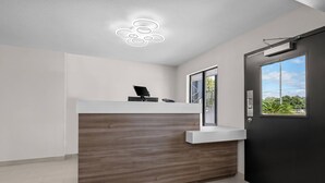 A reception area with a wooden reception desk, a white counter, a modern light fixture, and a window with a view of greenery. - Econo Lodge Biloxi Beach (Biloxi)