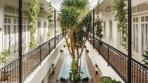 A covered outdoor swimming pool with a staircase leading up to it, surrounded by potted plants and outdoor furniture. - Brown Feather Batu Belig (Keroboken Kelod)