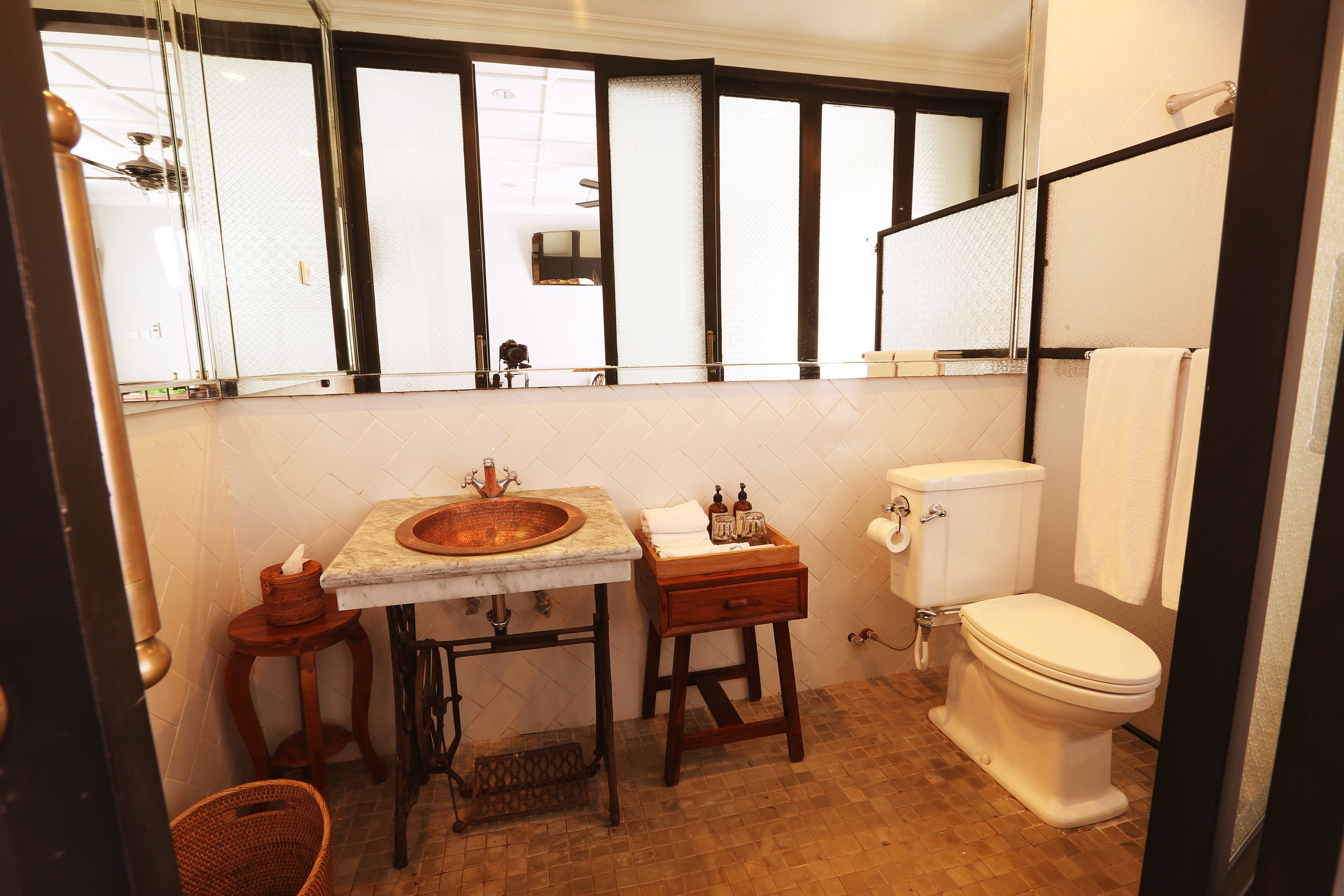 A bathroom with a sink, mirror, toilet, and a window with blinds.