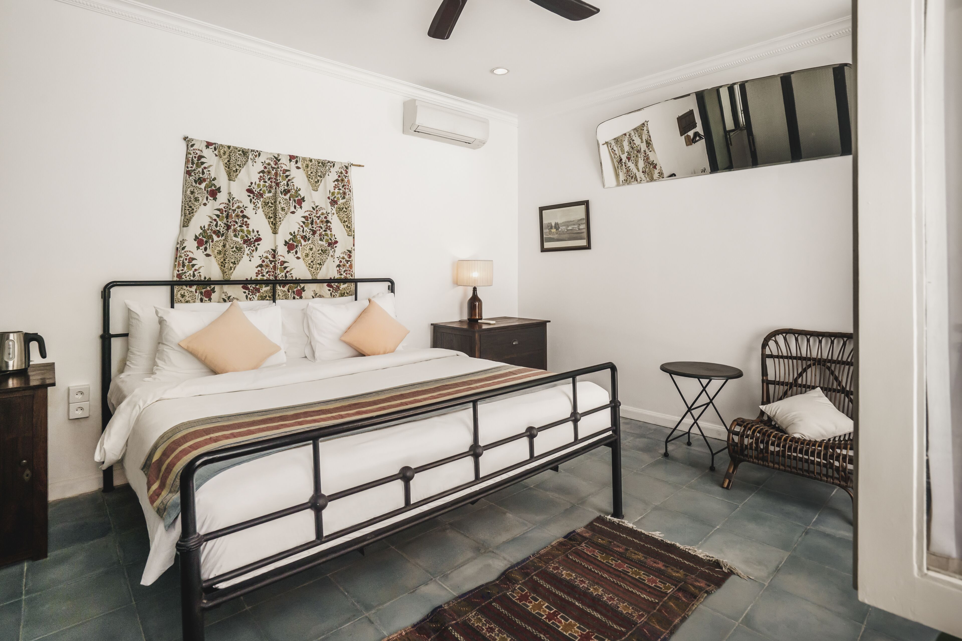 Un dormitorio con cama, mesita de noche, lámpara y una silla pequeña.