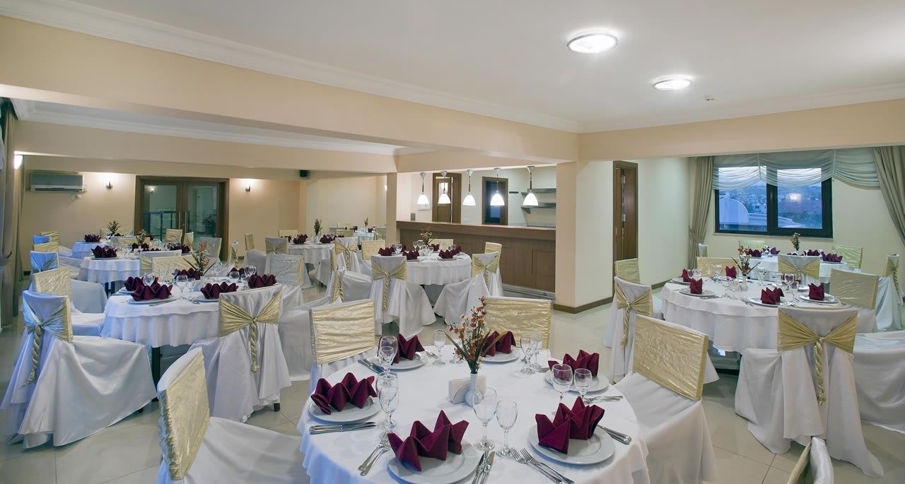 Una sala de banquetes amb taules rodones preparades per dinar, cadascuna amb estovells blancs, cintes daurades i serretes morades.