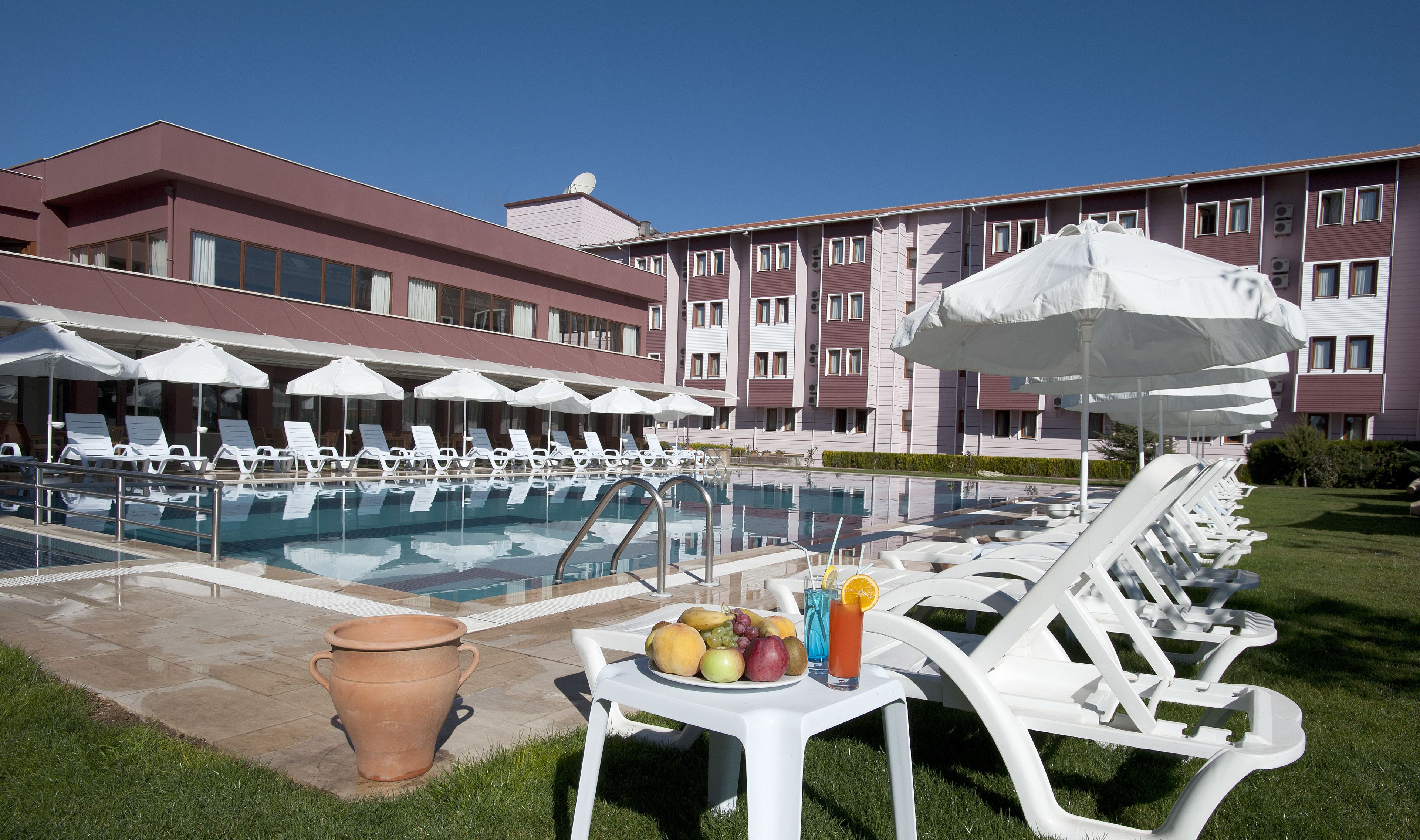 Zona junto a la piscina con sillones de descanso, sombrillas y una mesa con frutas y bebidas.