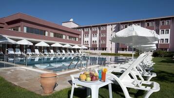 Zona junto a la piscina con sillones de descanso, sombrillas y una mesa con frutas y bebidas.