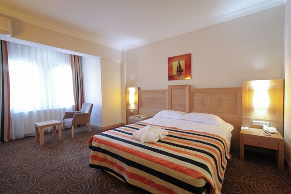 A hotel room with a large bed, a chair, a nightstand, and a painting on the wall.