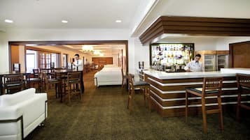 A hotel lobby with a bar area, multiple seating arrangements, and a reception desk.