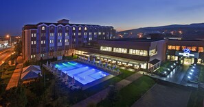A hotel with a swimming pool, outdoor seating, and a well-lit facade.