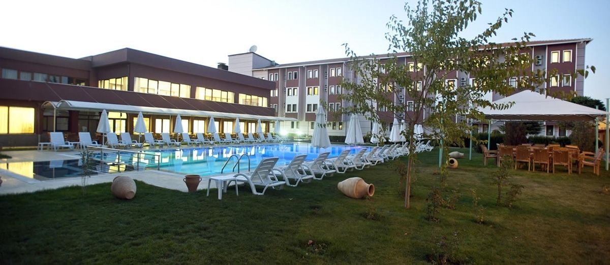 A hotel pool area with lounge chairs and umbrellas, a covered seating area, and a building with multiple windows.
