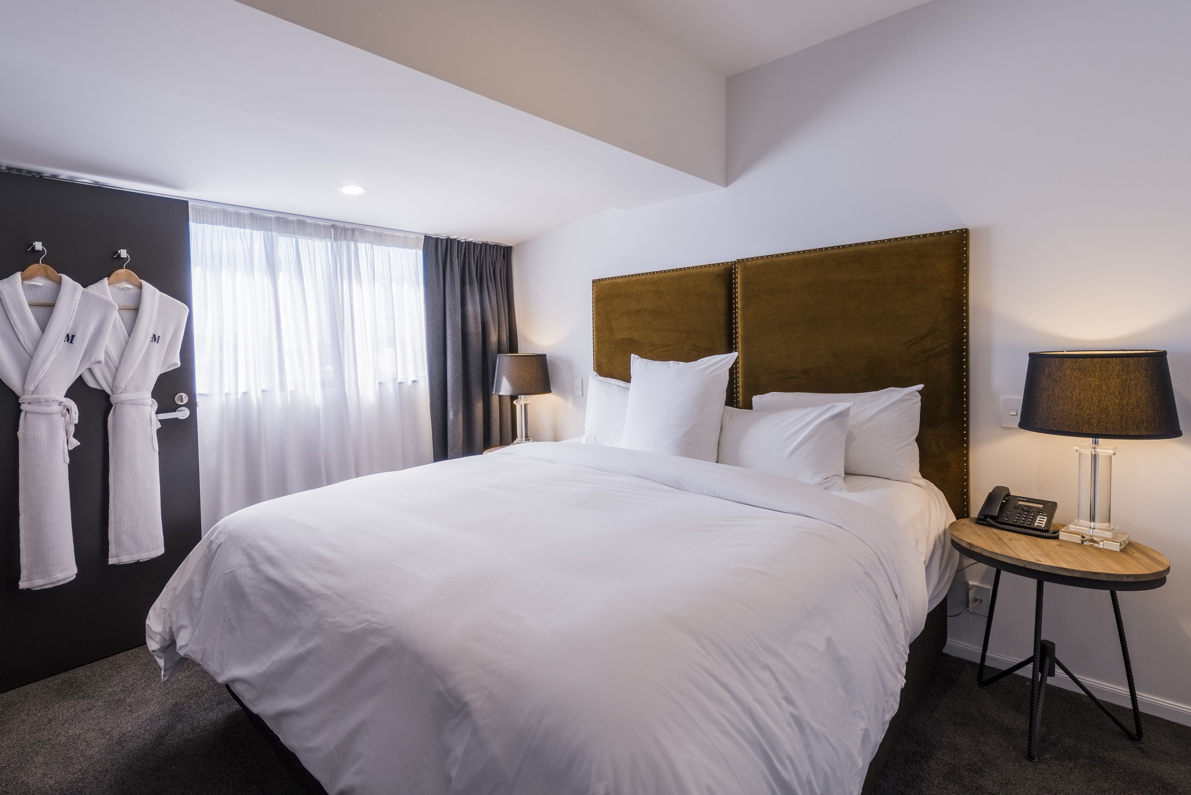 Una habitación de hotel con una cama grande, dos mesitas de noche, un armario y una ventana con cortinas.