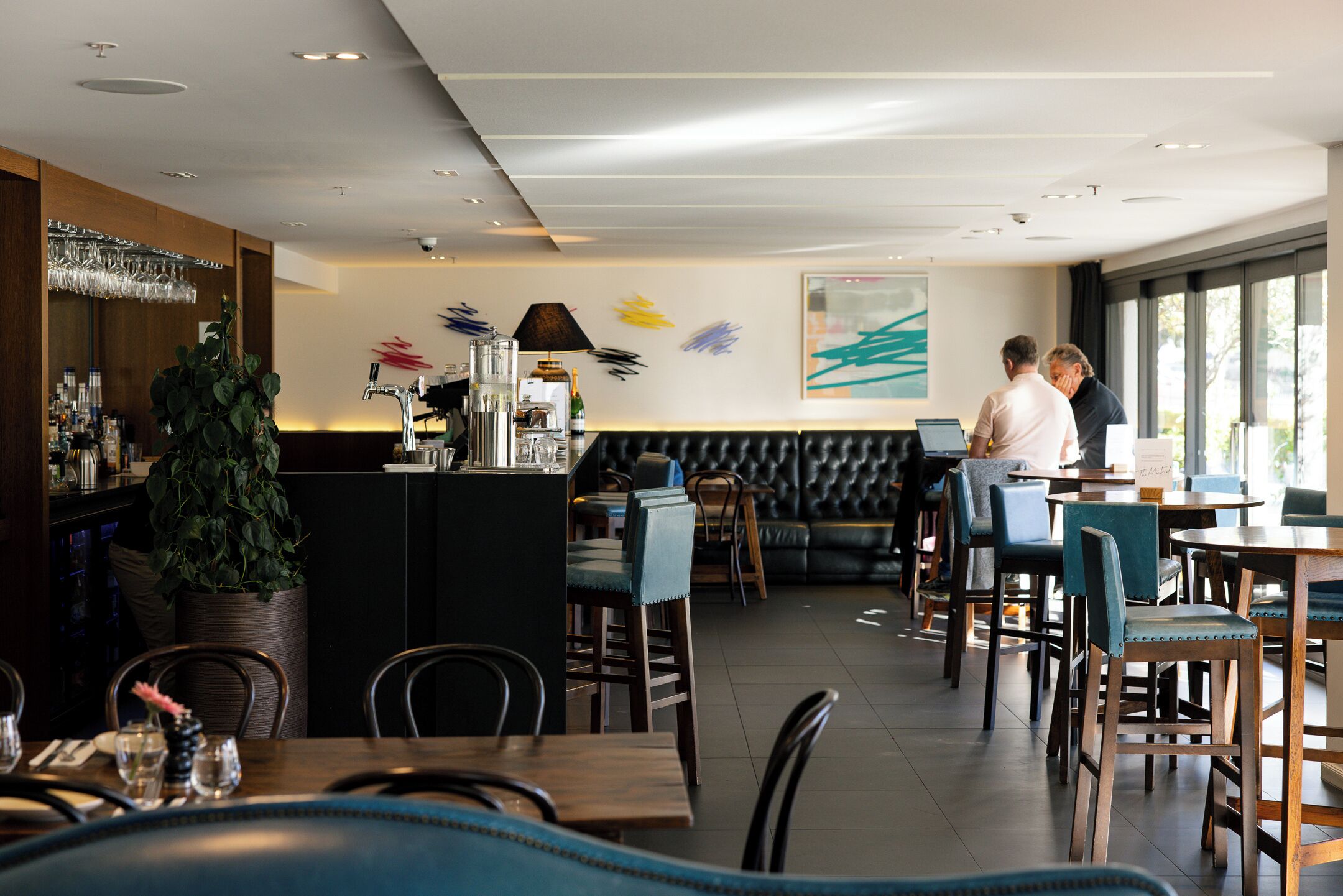 A modern restaurant with a bar area, seating arrangements, and a large window providing natural light.