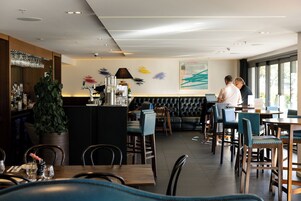 Un restaurante moderno con una zona de bar, diferentes disposiciones de asientos y un amplio ventanal que proporciona luz natural.