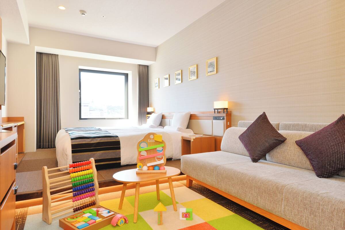 Een hotelkamer met een bed, een bank, een bureau, een stoel en een kleurrijke kinderspeelruimte.