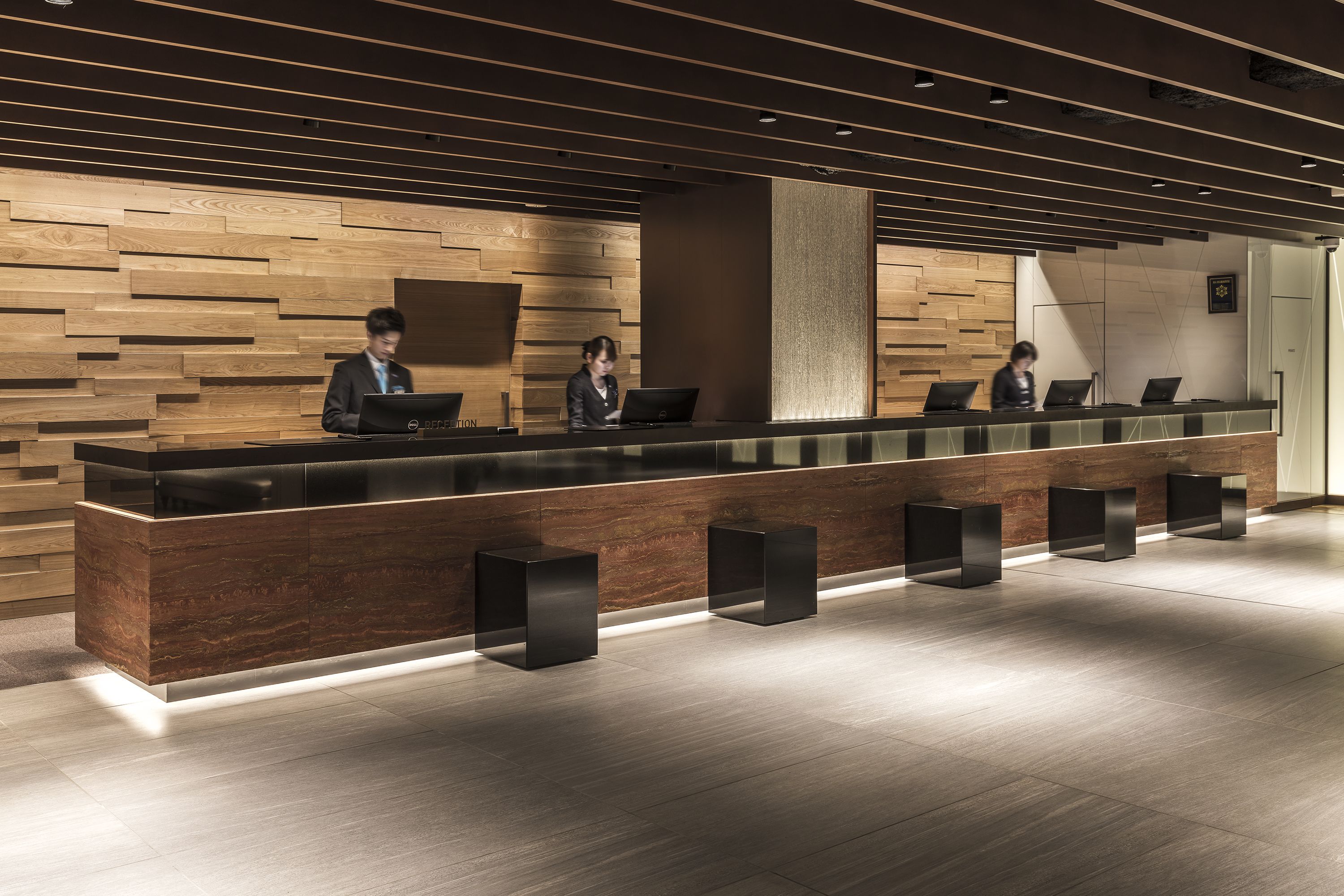 Een receptiebalie met drie medewerkers, houten lambrisering en een modern design.