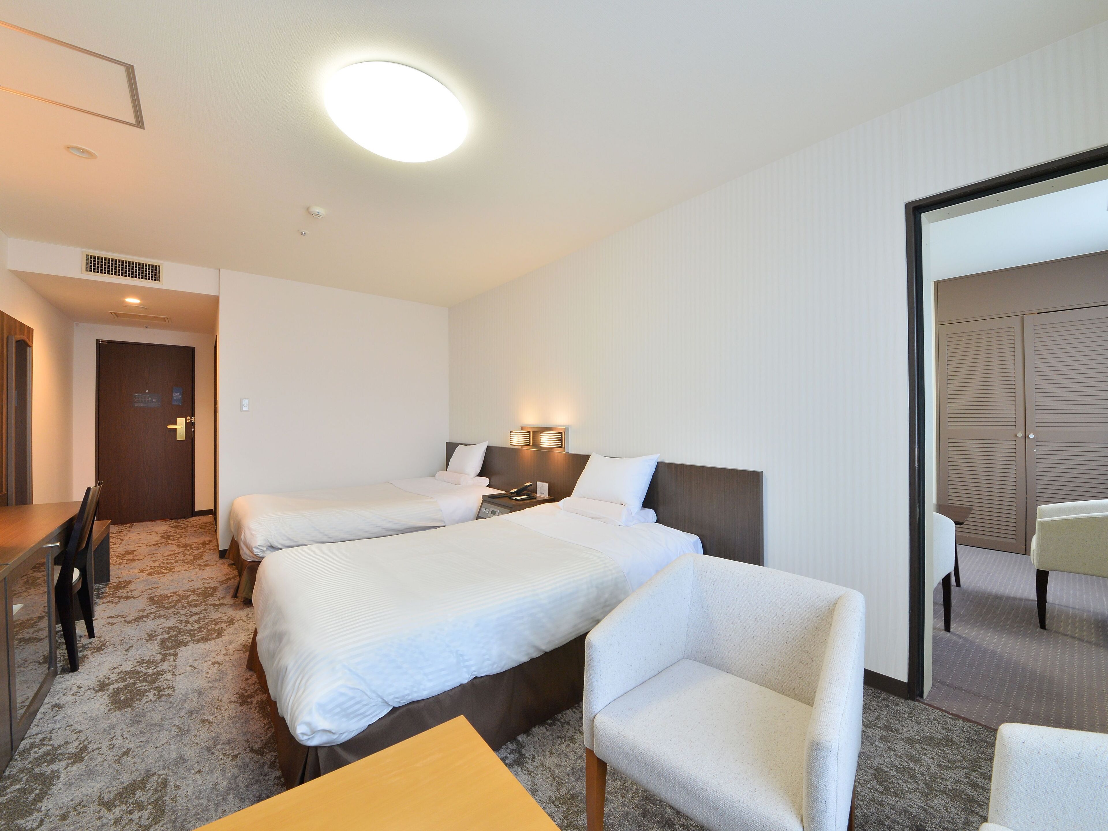 Ein Hotelzimmer mit zwei Betten, einem Schreibtisch, einem Stuhl und einem Spiegel.