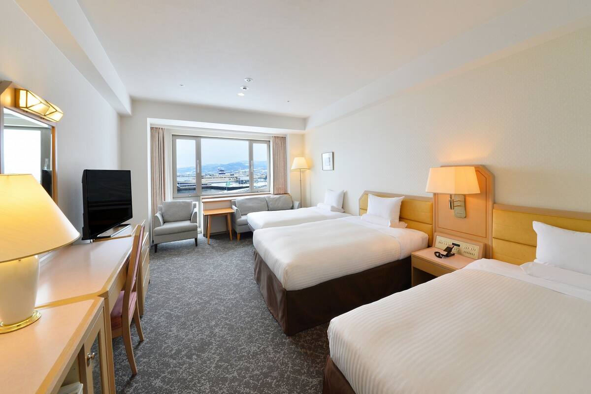 Een hotelkamer met twee bedden, een bureau, een televisie en een raam met uitzicht over de stad.