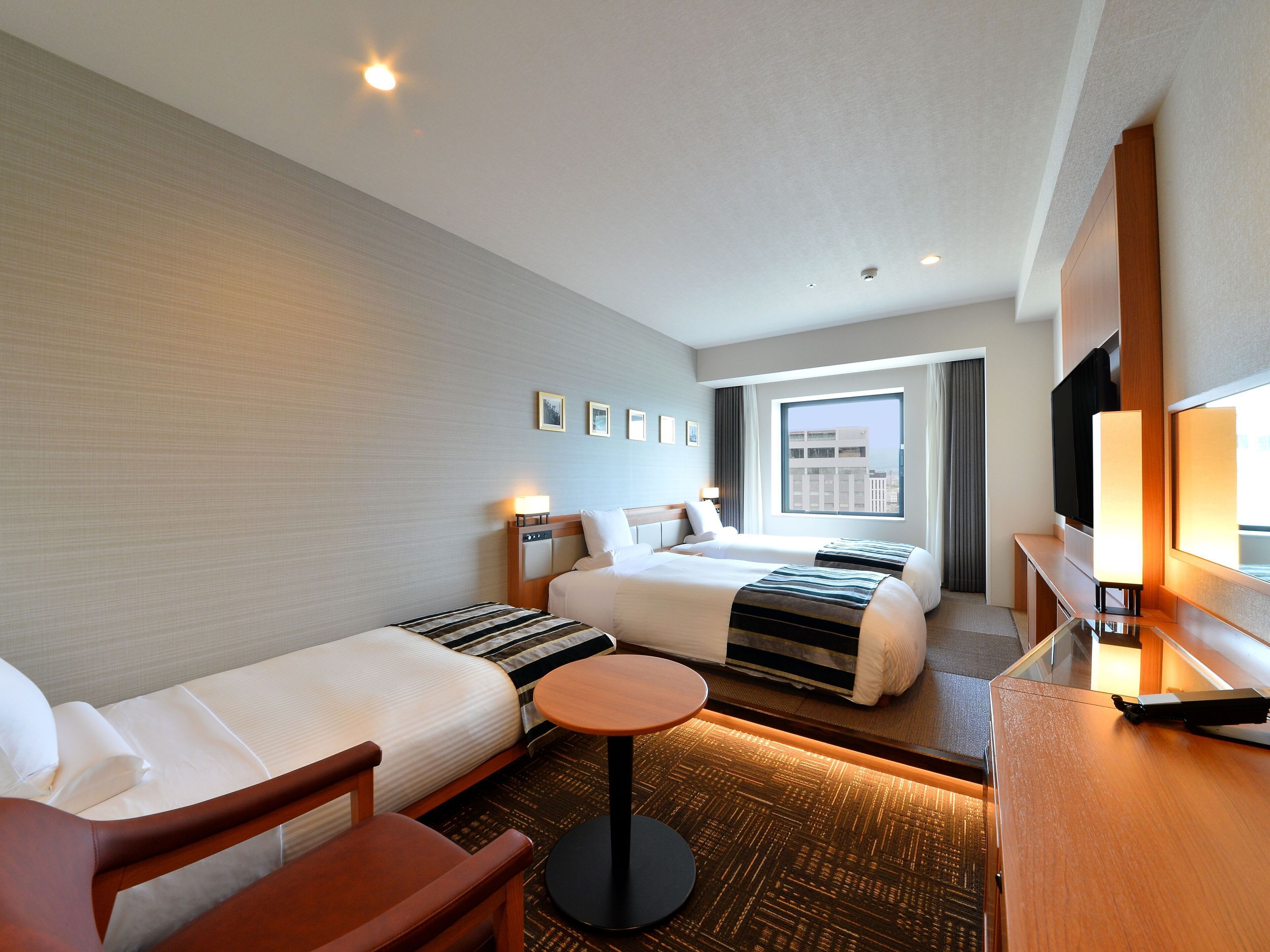 Une chambre d’hôtel avec deux lits, un bureau, une chaise, une petite table ronde et un téléviseur.