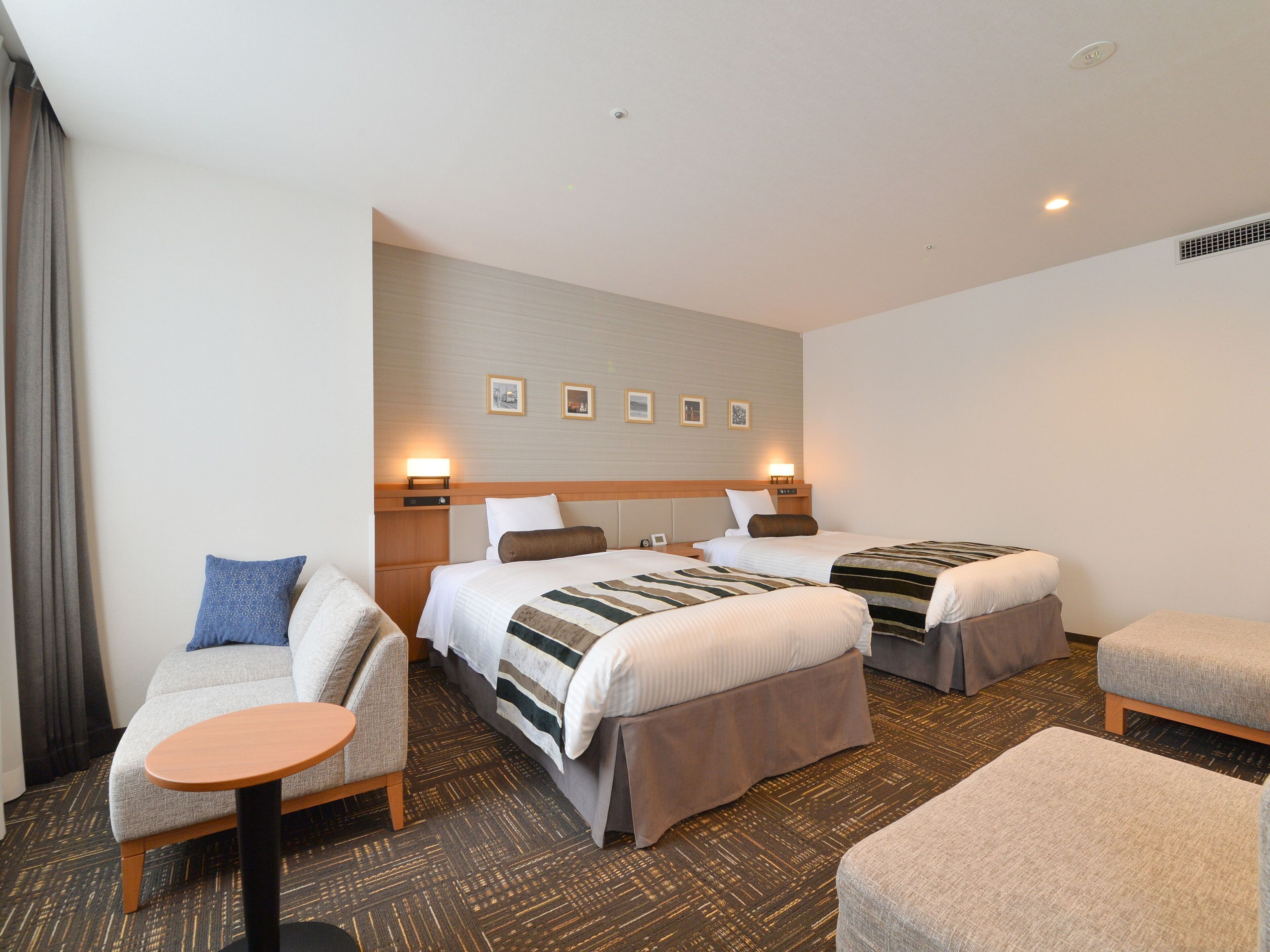 A hotel room with two beds, a sofa, a small table, and a carpeted floor.