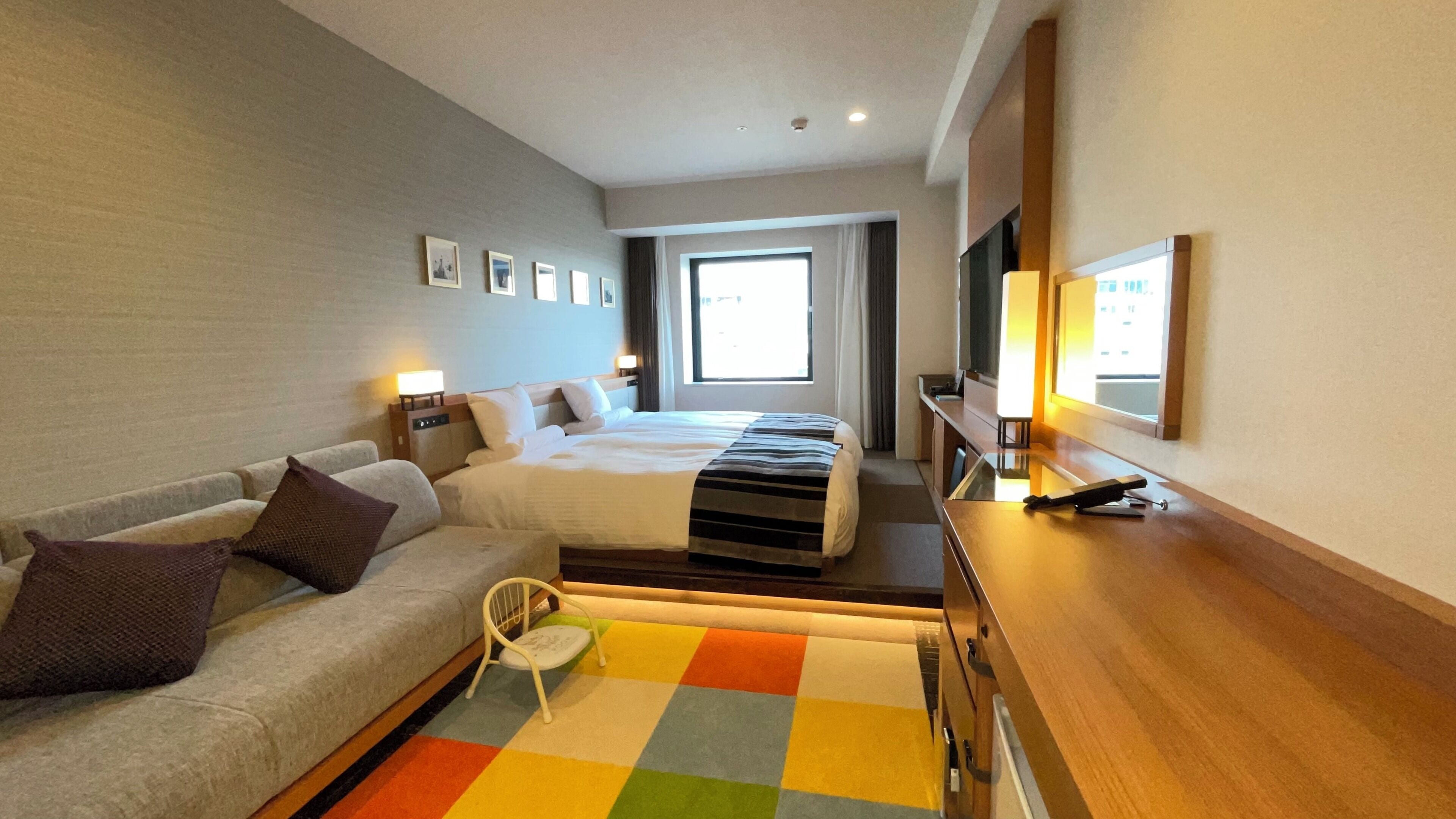 A hotel room with a bed, a sofa, a small table, and a TV.