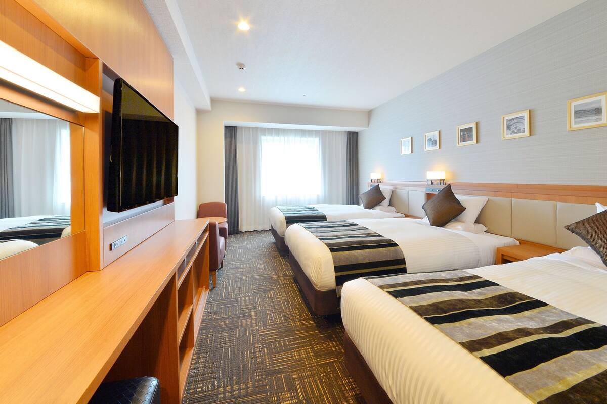 Een hotelkamer met twee bedden, een bureau, een televisie en een groot raam met gordijnen.