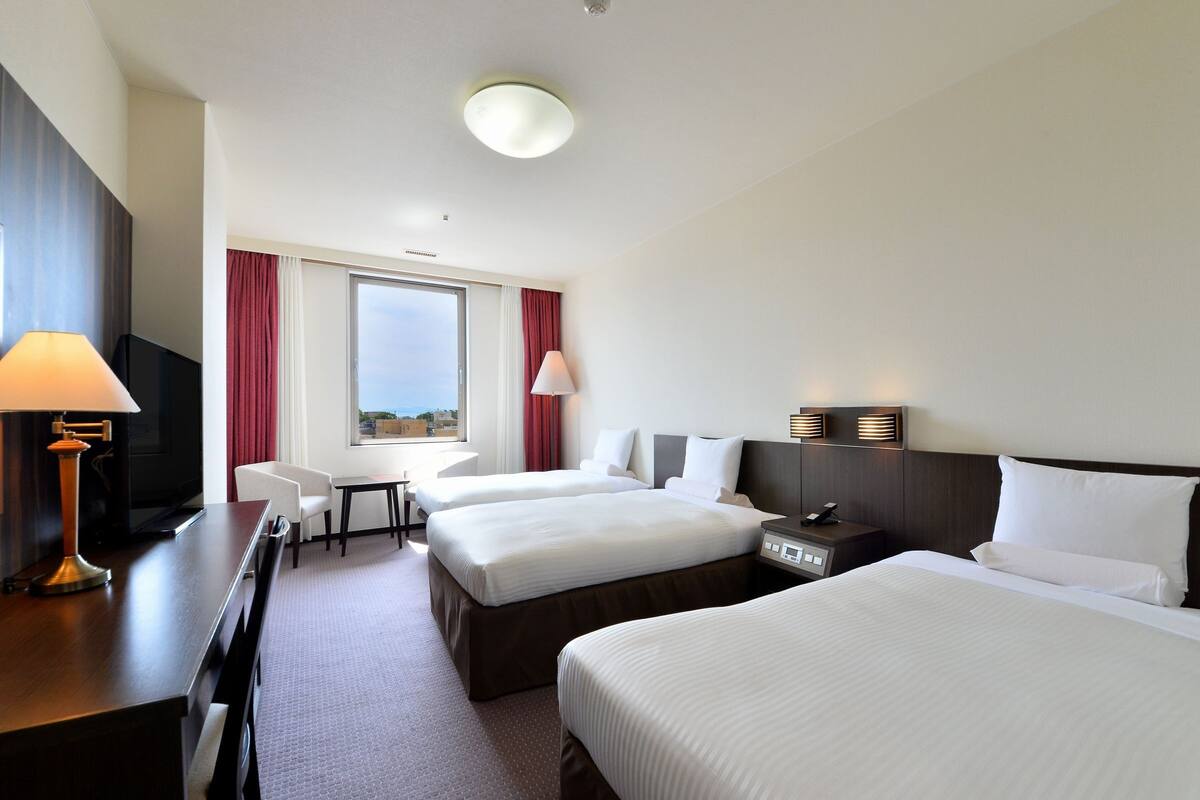 Een hotelkamer met twee bedden, een bureau met lamp, een televisie, een raam met uitzicht en een nachtkastje met telefoon.