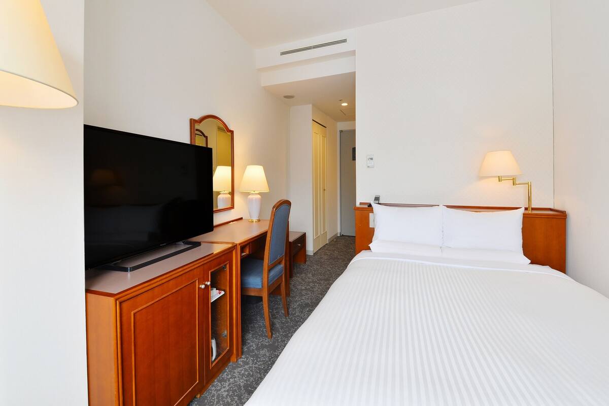 Een hotelkamer met een bed, een bureau met een televisie, een stoel en twee bedlampen.