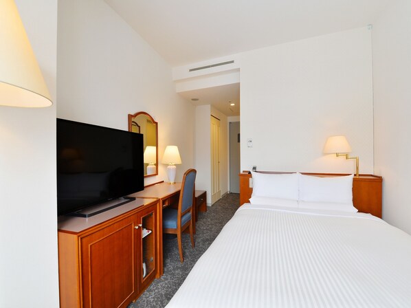 Una habitación de hotel con cama, escritorio, televisor, silla y dos lámparas de noche.