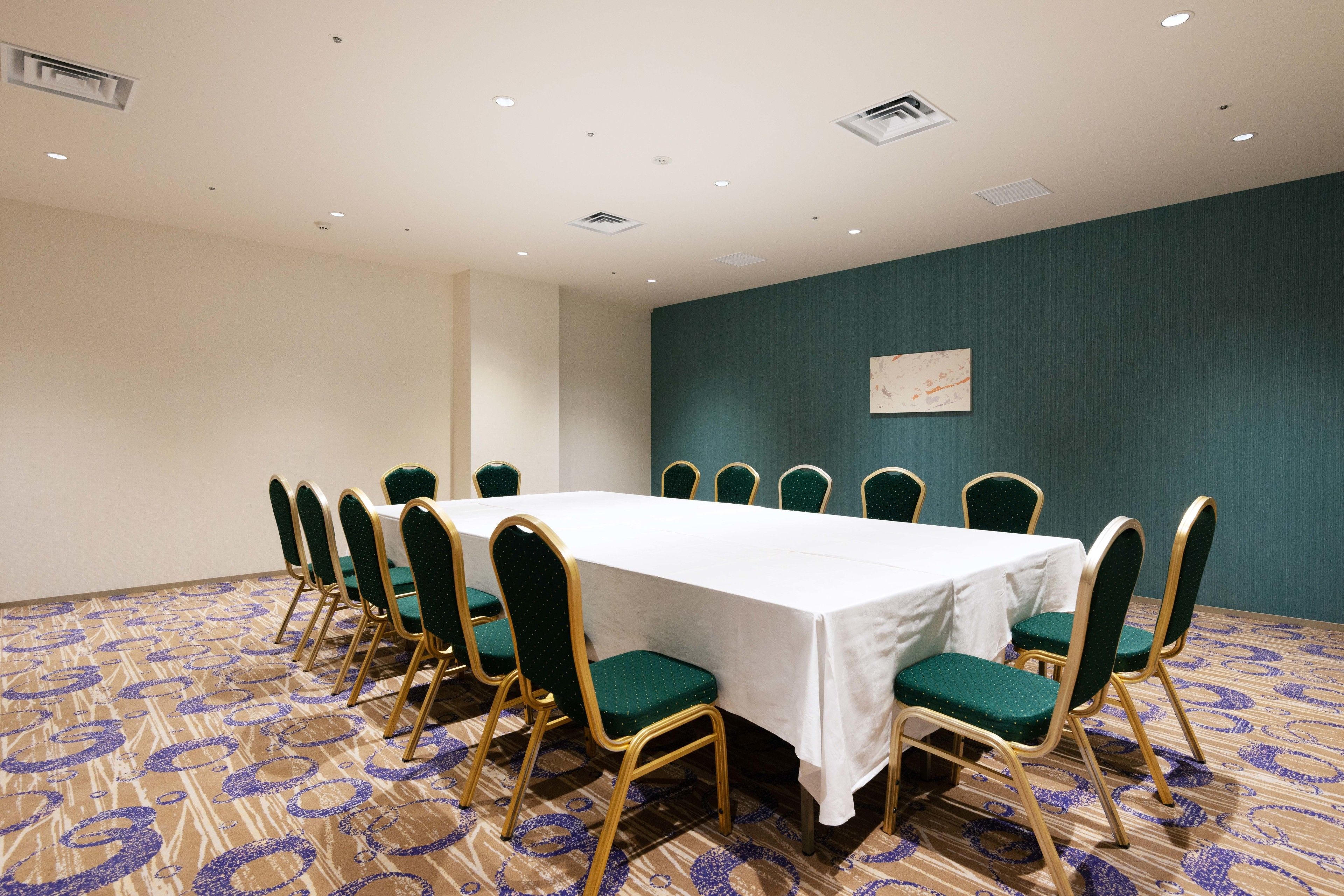 A conference room with a long table, green chairs, and a patterned carpet.