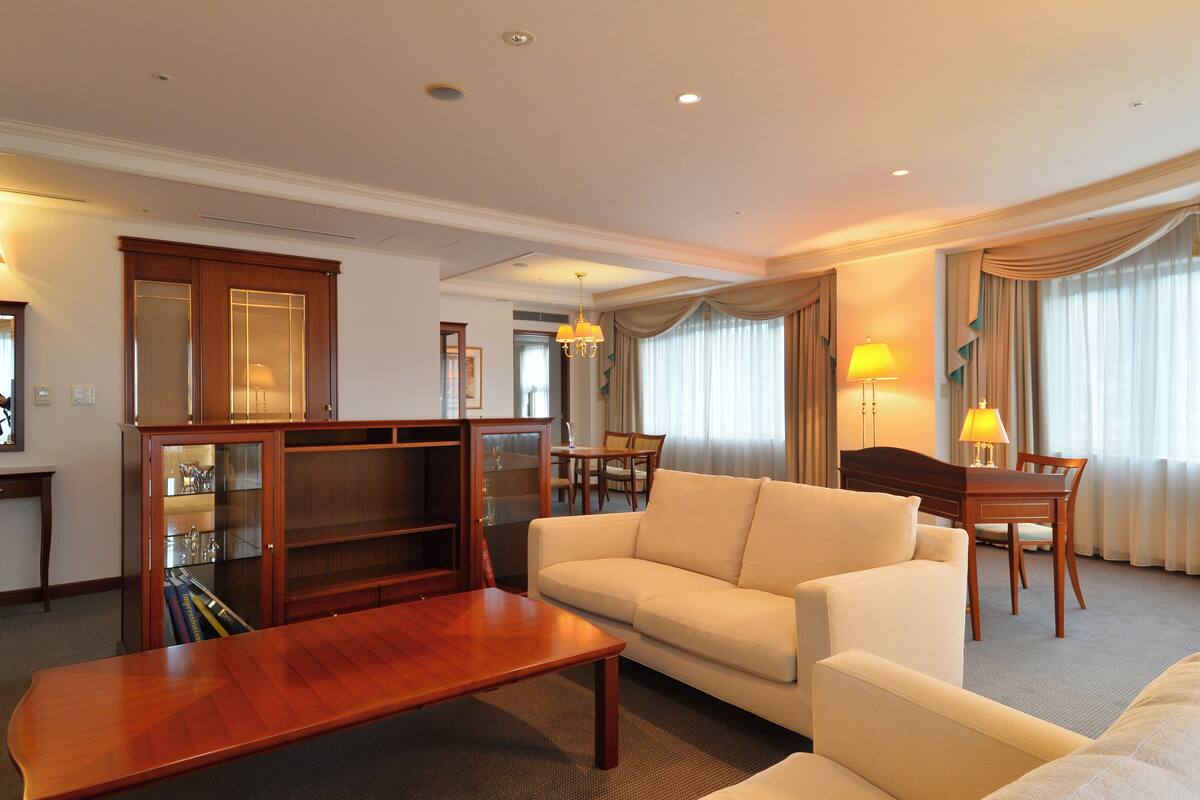 Een hotelkamer met een bank, een houten salontafel, een eettafel met stoelen, een kast met glazen deuren en een kroonluchter.