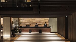 A modern reception area with a wooden reception desk, a large potted plant, and a long, well-lit corridor. - Hakodate Kokusai Hotel (Hakodate)