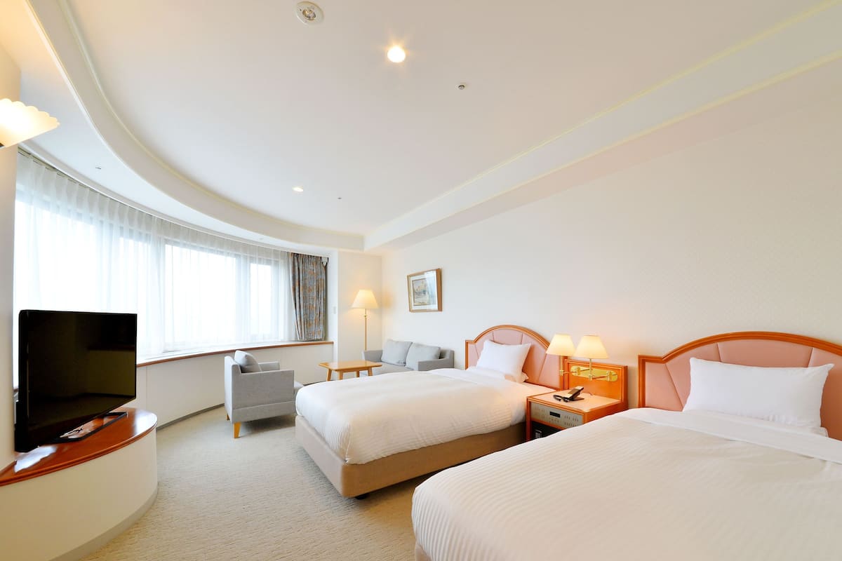 Een hotelkamer met twee bedden, een televisie, een bureau en een raam met gordijnen.