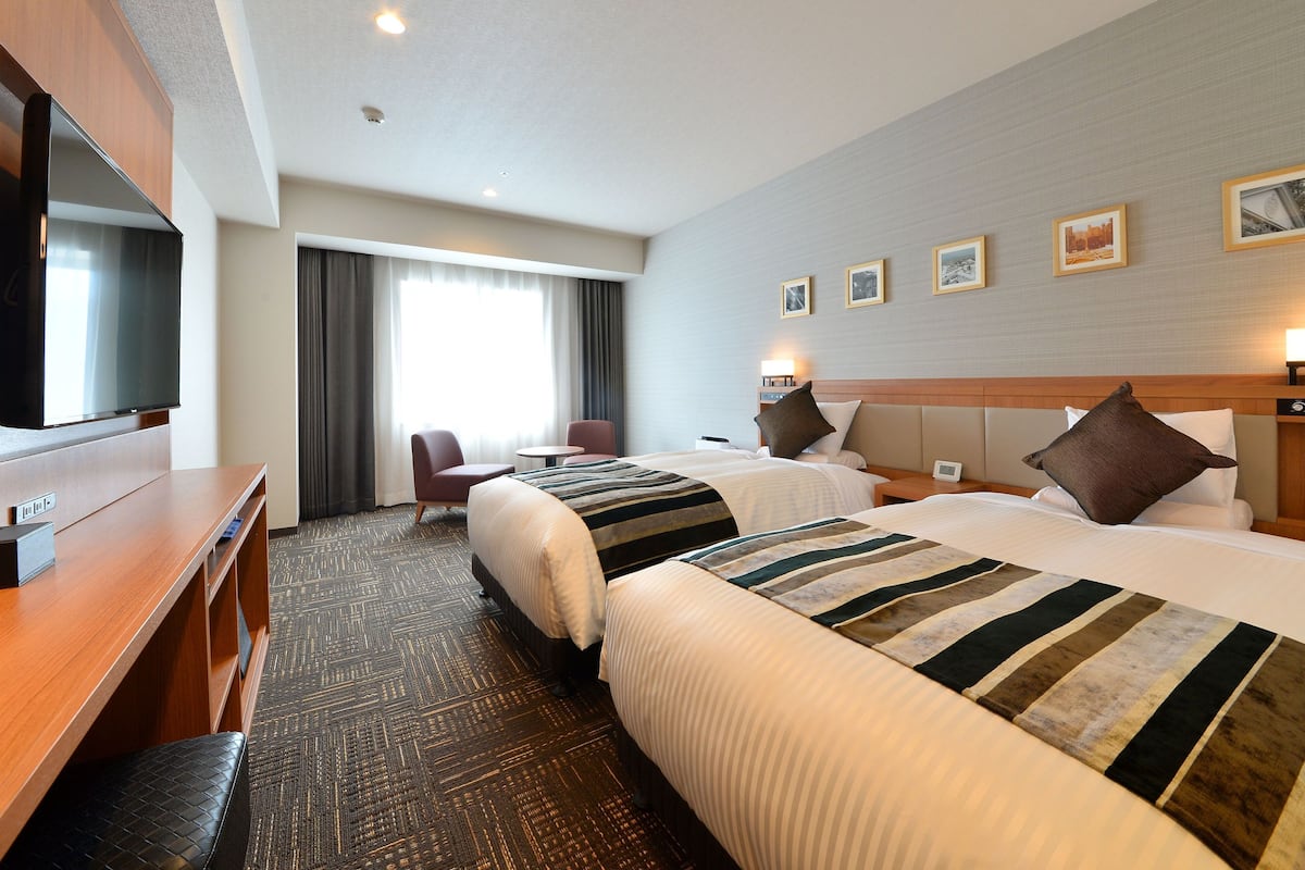 Een hotelkamer met twee bedden, een bureau, een televisie en een raam met gordijnen.
