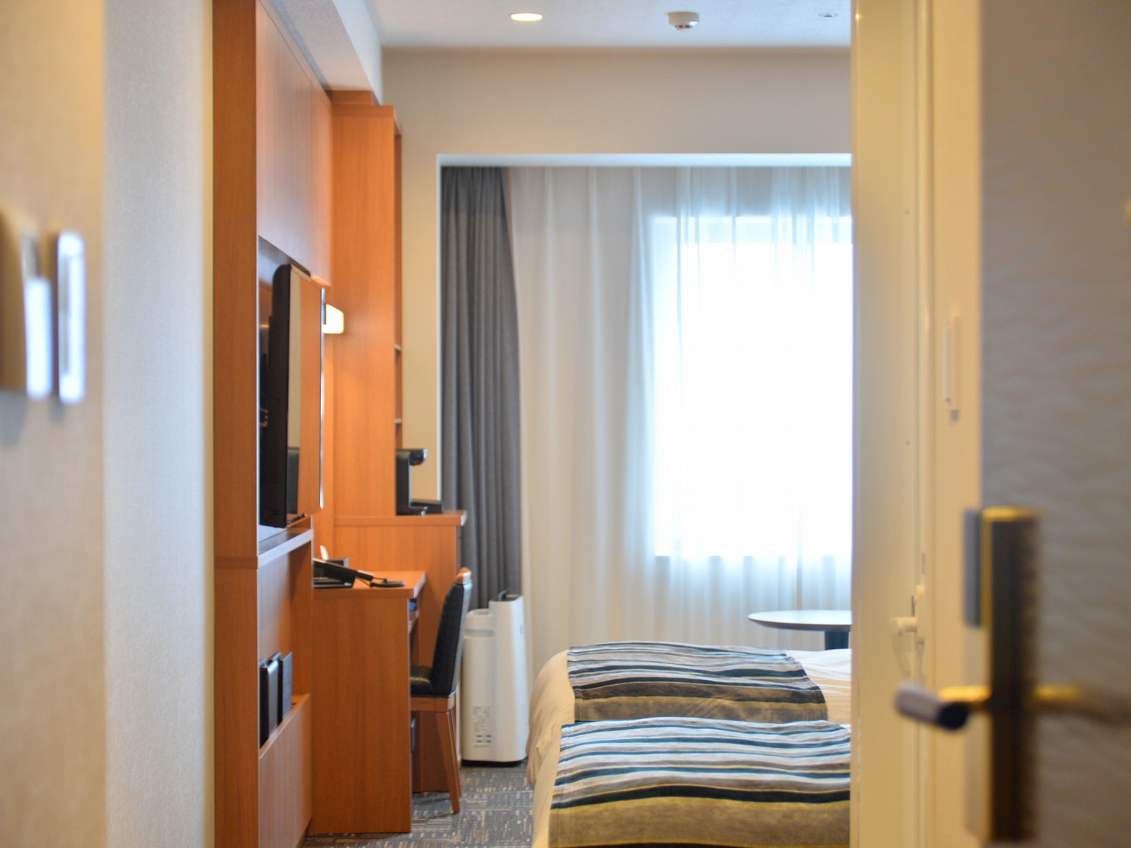 A hotel room with a bed, a desk, a chair, a television, and a window with curtains.