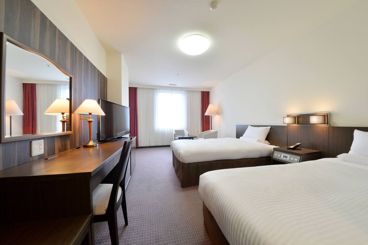 Een hotelkamer met twee bedden, een bureau, een stoel, een televisie en een grote spiegel.