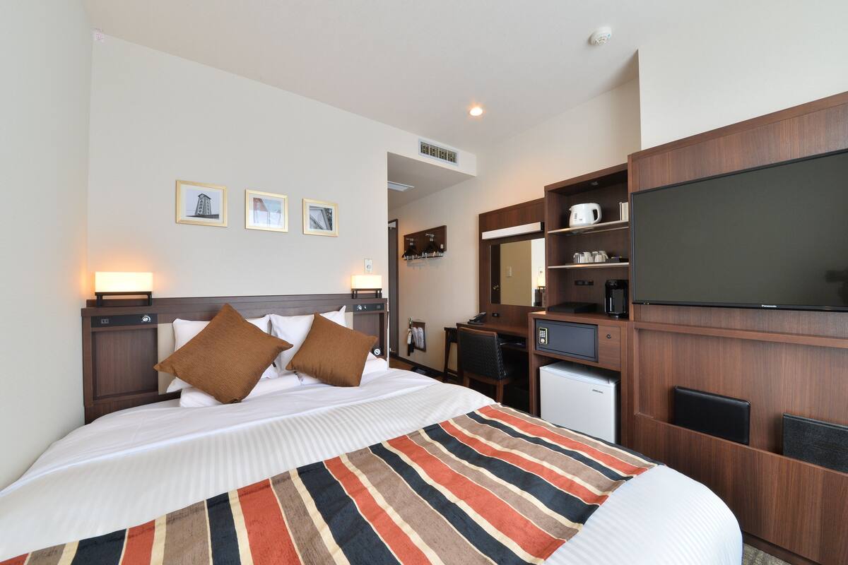 Een hotelkamer met een bed, nachtkastjes, een bureau, een televisie en een koffiezetapparaat.