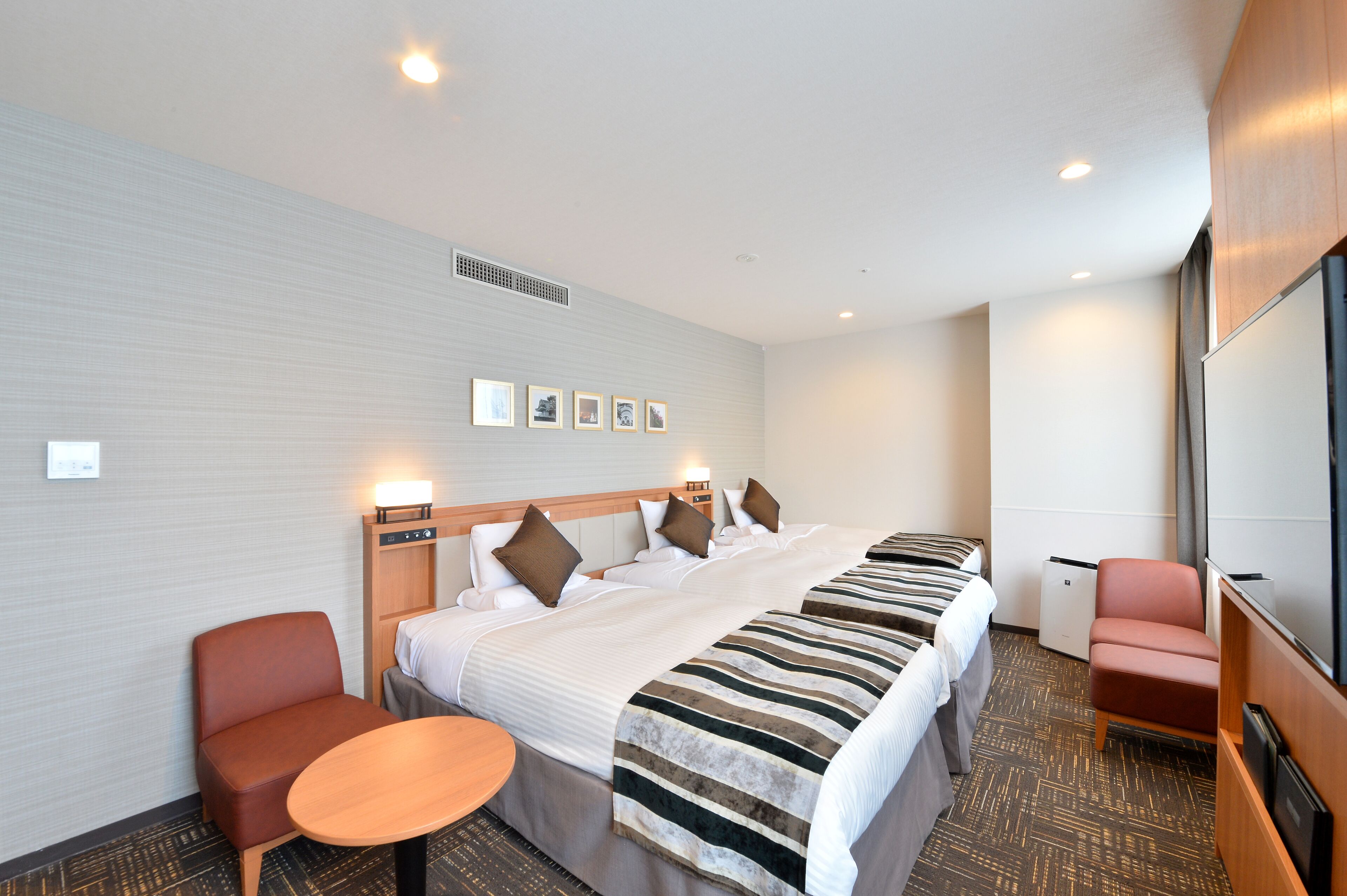 A hotel room with a large bed, two bedside tables, a chair, a small table, and a television.