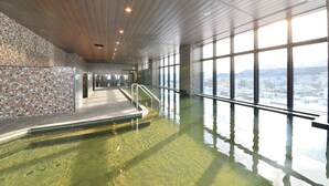 An indoor swimming pool with a view of a cityscape through large windows. - Hakodate Kokusai Hotel (Hakodate)