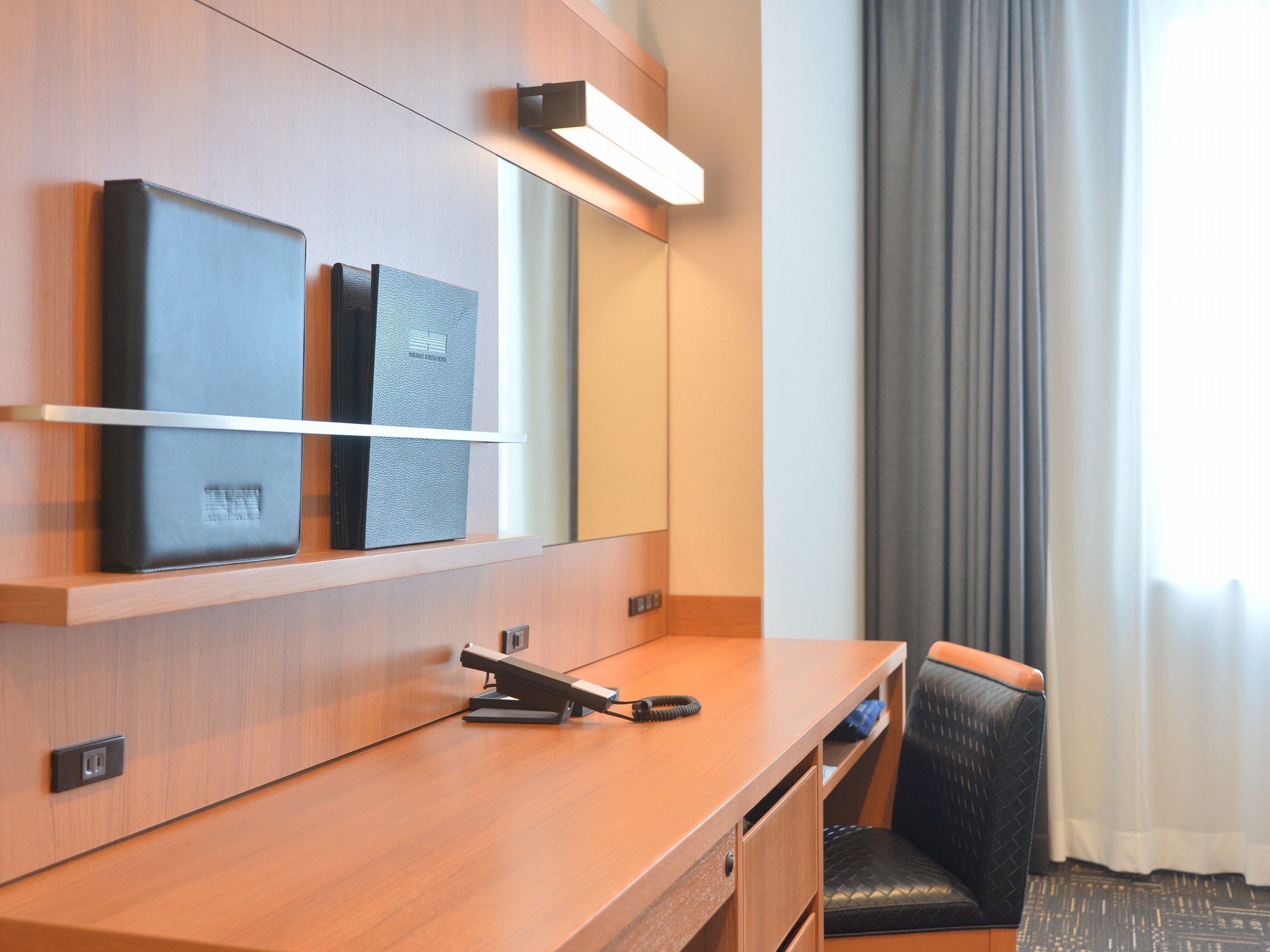 Une chambre d’hôtel équipée d’un bureau en bois, d’un téléphone, d’une télévision à écran plat et d’un miroir.