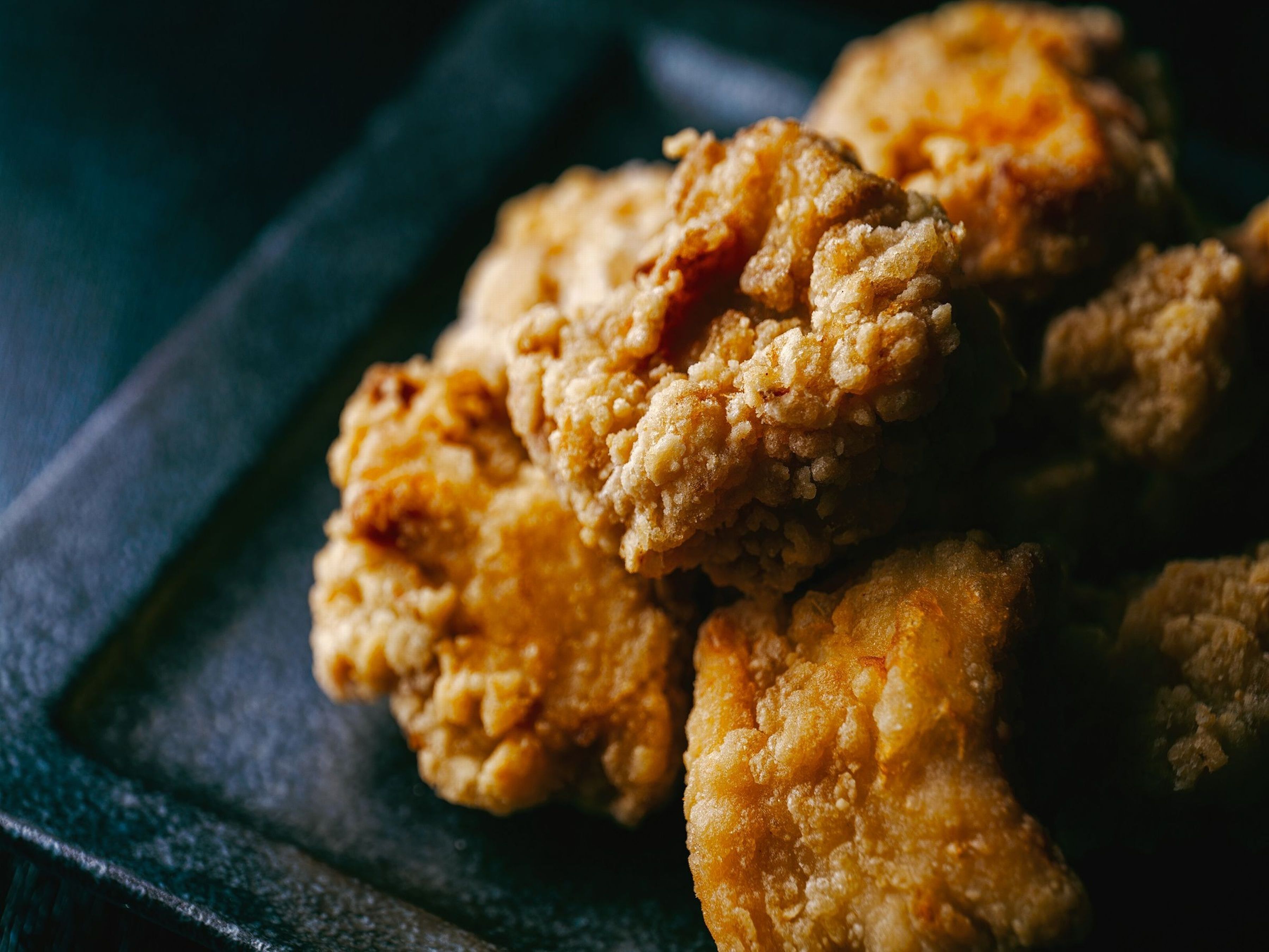 A close-up of fried chicken pieces on a dark plate.
