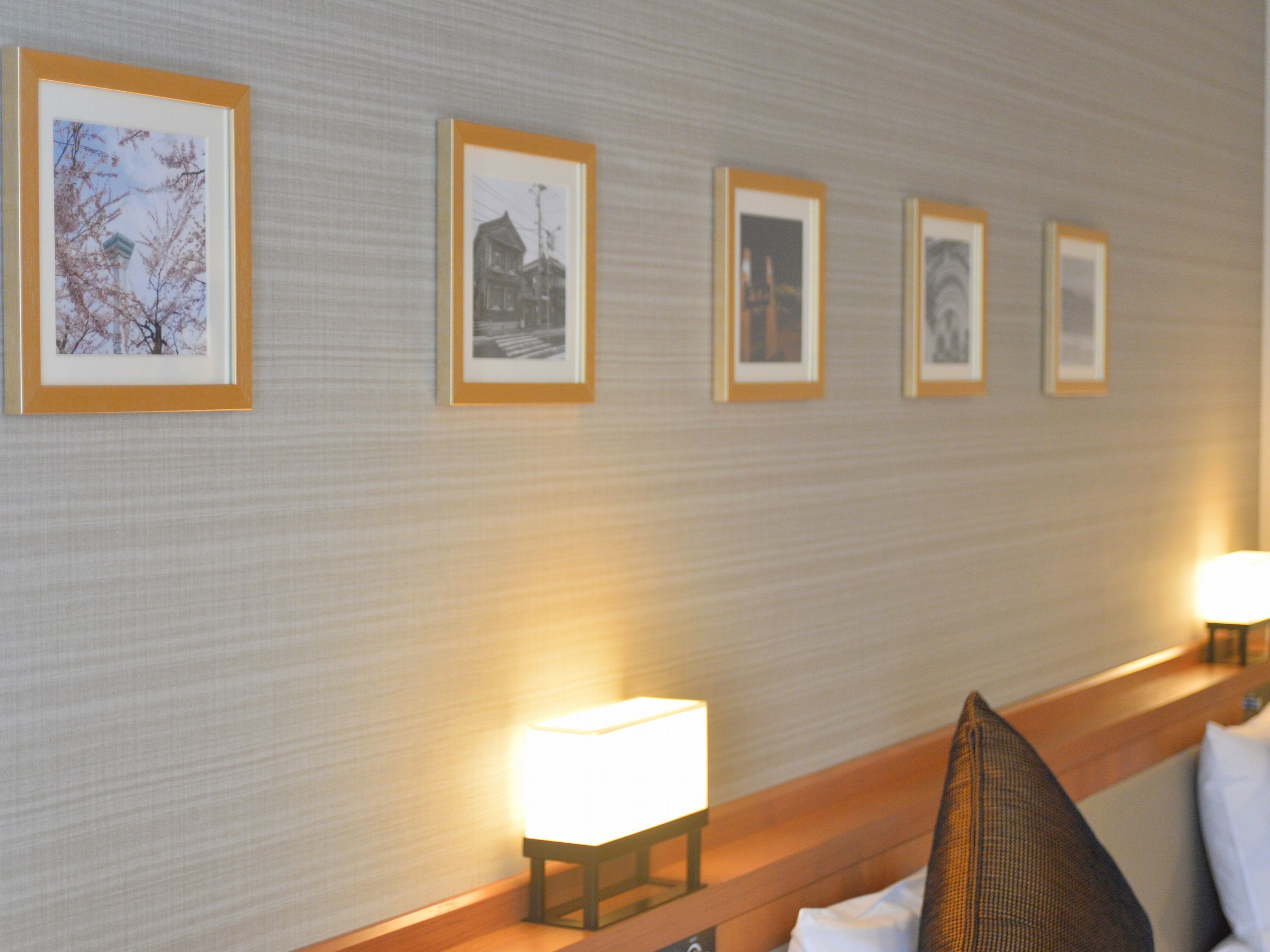 A hotel room with a bed, a nightstand, and a wall with framed pictures.