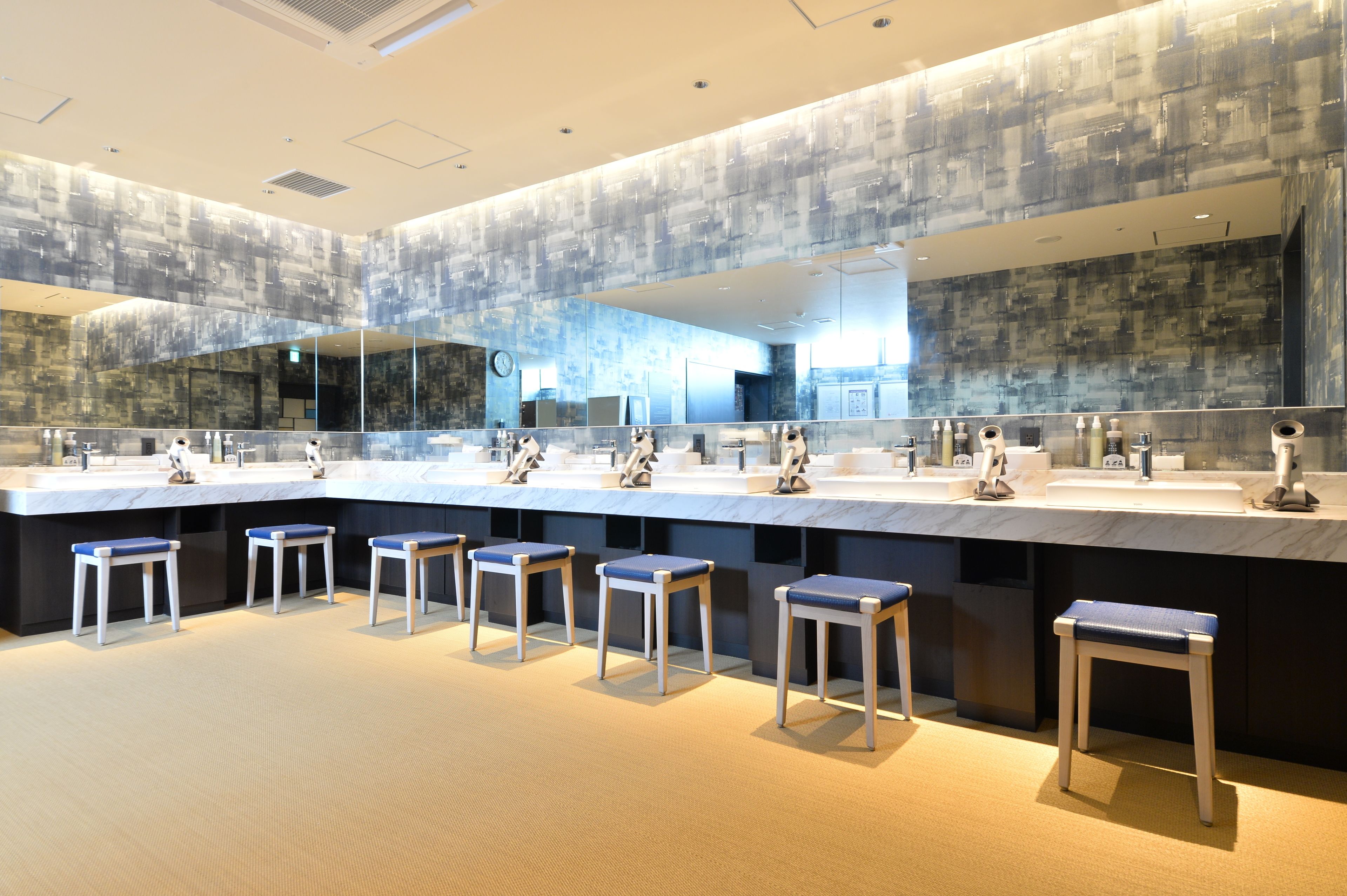 A modern bathroom with multiple sinks, mirrors, and bar stools.