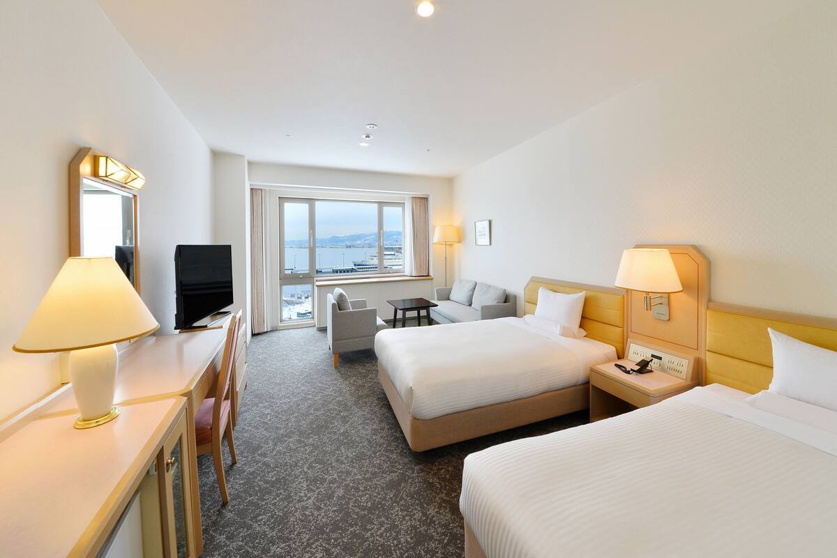 Een hotelkamer met twee bedden, een bureau met een televisie, een stoel en uitzicht op de zee.
